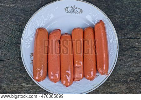 Food Of Six Red Fresh Sausages In A White Plate On A Gray Table