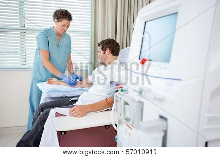 Mid adult female nurse injecting patient for renal dialysis treatment in hospital room