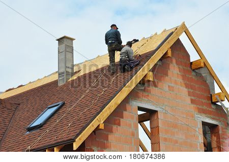 Roofing Construction and Building New Brick House with Modular Chimney Skylights Attic Dormers and Eaves Exterior. Roofers Install Repair Asphalt Shingles or Bitumen Tiles on the Rooftop Outdoor.