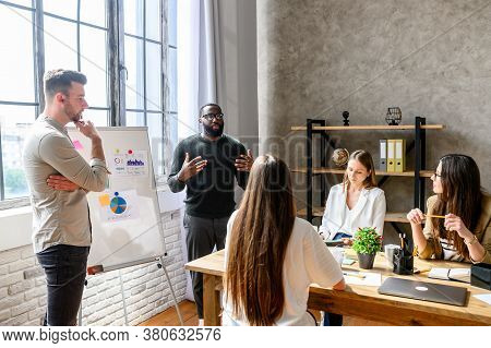 A Team Of Young And Successful Employees Listen To Progress Report From Male Afro-american Employee 