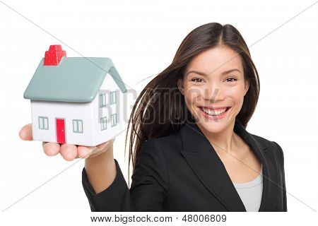 Real estate agent selling home holding mini house. Female realtor in business suit showing model house smiling happy isolated on white background. Multiracial Caucasian / Chinese Asian woman agent.