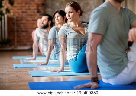 fitness, sport and healthy lifestyle concept - group of people doing yoga seated spinal twist pose in gym or studio