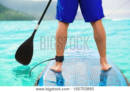 Paddle board man doing stand-up paddleboard on ocean. Athlete paddleboarding on SUP surf board on Hawaii beach travel. Closeup of legs standing on board.