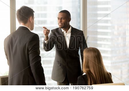 Angry african-american businessman threatens colleague, conflict between male workers at workplace, bullying and discrimination, black boss blames white employee responsible for failure, your fault