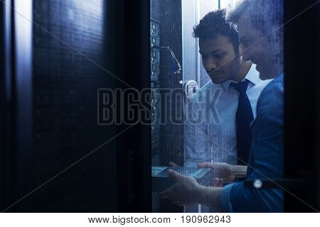 Informational technology. Handsome skillful male technician standing together near the data server and installing a blade server while working in the server room