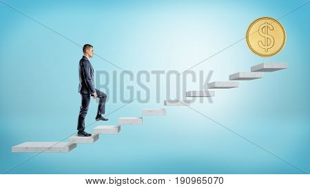 A businessman on blue background walking up a concrete block stairs where a giant golden coin stands on the top. Roadway to wealth. Get rich. Monetary motivation.