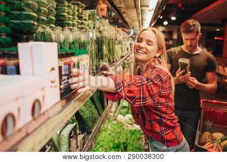 Young Couple In Grocery Store. Woman Reach Ahnd To Box And Smile. Man Stand Behind And Look At Parsl