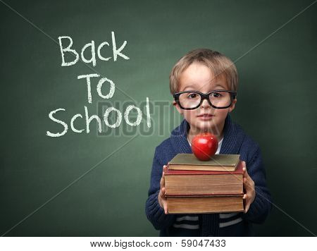 Young child holding stack of books and back to school written on chalk blackboard