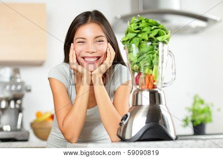 Green smoothie woman making vegetable smoothies with blender. Healthy eating lifestyle concept portrait of beautiful young woman preparing drink with spinach, carrots, celery etc at home in kitchen.