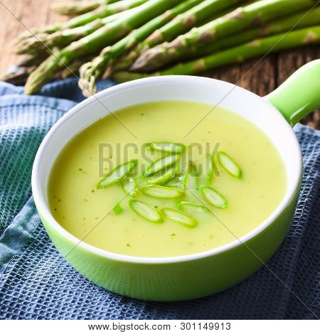 Cream Of Green Asparagus Soup In Bowl, Garnished With Sliced Asparagus On Top, Fresh Asparagus In Th