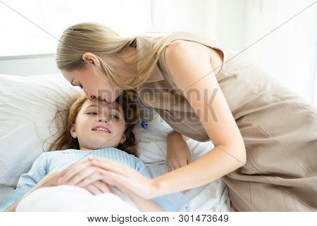 Sick Kid Girl With Laying In Bed At Hospital And Mother's Hand Holding Together And Mom Kiss Her To 