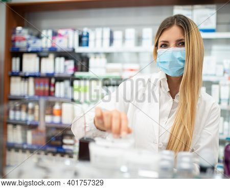 Young female pharmacist checking the inventory in a pharmacy while wearing a coronavirus covid mask