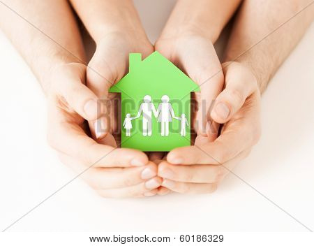 real estate and family home concept - closeup picture of male and female hands holding green paper house with family