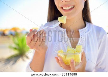 Pineapple - woman eating sliced Hawaiian pineapple fruit as a healthy snack from take away bowl.