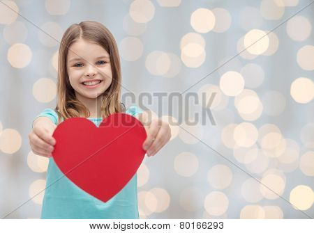 love, charity, holidays, children and people concept - smiling little girl with red heart over lights background