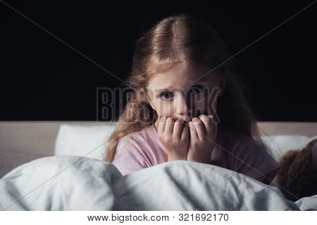 Scared Child Looking At Camera While Sitting On Bedding Isolated On Black