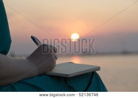 Woman writing in her diary at sunset