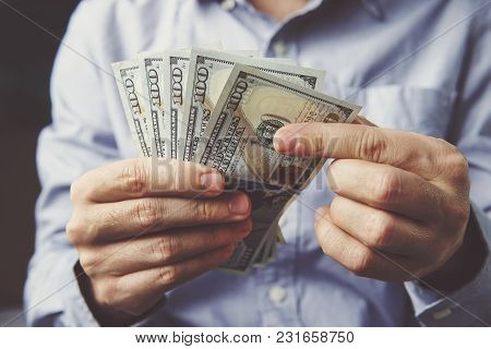 Hands Counting Dollar Banknotes On Dark Wooden Surface. Office Worker Considers The Salary In Dollar