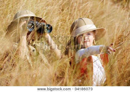 Happy young safari adventure children playing outdoors in the grass with binoculars and exploring together as brother and sister.