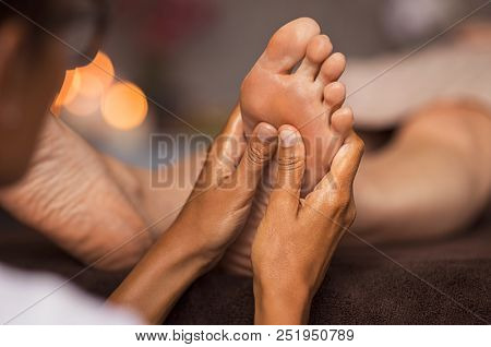 Closeup of masseuse doing foot reflexology to woman at spa. Therapist hands doing foot massage at wellness center. Woman receiving a feet massage at health spa.