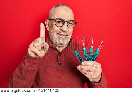 Handsome mature man holding picklock to unlock security door smiling with an idea or question pointing finger with happy face, number one 