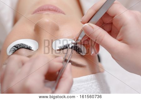 Permanent makeup. Eyelash Extension Procedure. Woman Eye with Long Eyelashes. Professional stylist lengthening female lashes. Eyelash extension procedure - master and a client in a beauty salon