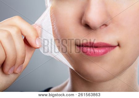 Portrait Of A Beautiful Young Woman Removing Peeling Mask From Her Face