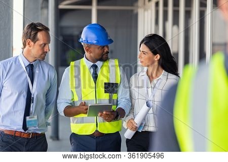 Team of construction workers discussing project details with executive supervisor. Group of architects and civil engineers inspecting construction site. Structural engineer and architect discussing.