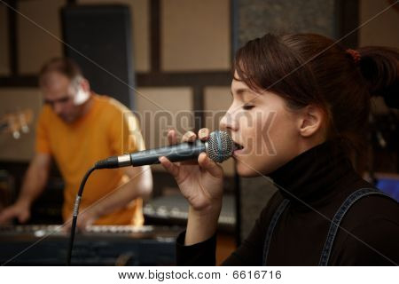 vocalist girl is singing in studio. keyboard player in out of focus