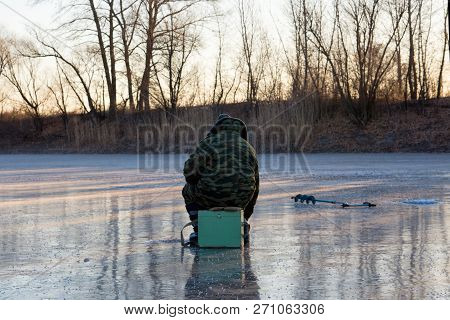 Beautiful Landscape Of Forest Lake. Fisherman Sitting On The Ice. The First Fishing From The Ice.