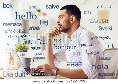 translation, business, and technology concept - male translator or businessman with laptop computer thinking at office over greeting words in different foreign languages