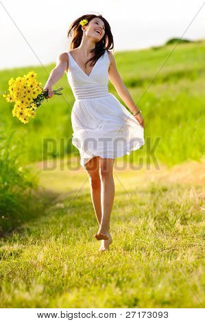 Sincera pulando despreocupada adorável mulher no campo com flores, pôr do sol de Verão.