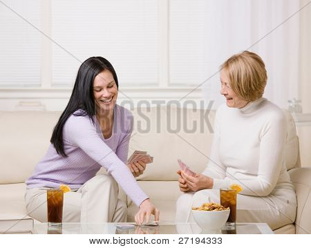 Adult mother and daughter playing cards and enjoying ice tea and snacks at home