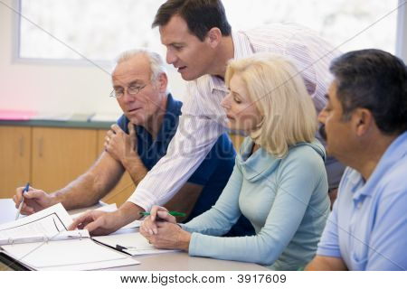 Estudantes adultos na classe com o professor ajudando (foco seletivo)