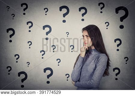 Puzzled Young Woman Has Multiple Questions, Keeps Hand Under Chin, Thoughtful Gesture, Looking Ahead