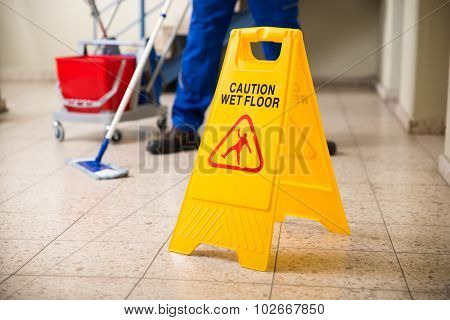 Worker Mopping Floor With Wet Floor Caution Sign