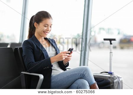 Airport business woman on smart phone at gate waiting in terminal. Air travel concept with young casual businesswoman sitting with hand luggage suitcase. Beautiful young mixed race female professional