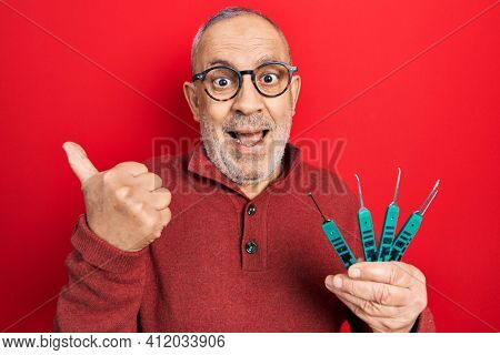 Handsome mature man holding picklock to unlock security door pointing thumb up to the side smiling happy with open mouth 