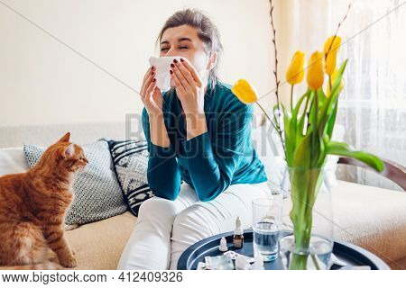 Spring Allergy. Woman Sneezing Because Of Tulips Flowers Surrounded With Pills And Nasal Drops Sitti