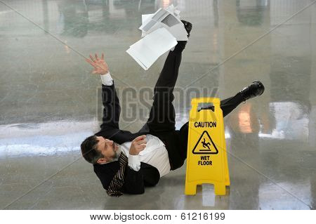 Senior businessman falling on wet floor in front of caution sign