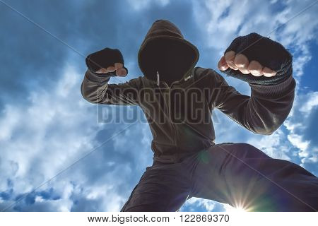 Violent attack unrecognizable hooded male criminal kicking and punching victim on the street.