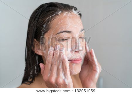 Skincare woman washing face in shower foaming facewash soap scrub on skin. Asian female adult cleaning body showering in hot water at home on in hotel as morning routine. Enjoying relaxing time.