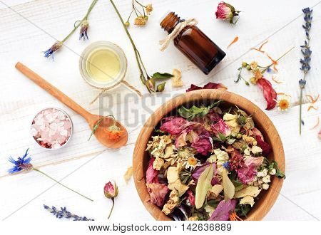 Herbal blend of various dried medicinal flowers, essential oil, bottle, sea salt. Natural skincare. Top view, focus on wooden bowl with colorful plants.