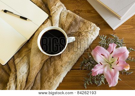 Wooden desk with a cup of coffee, notebook and flower