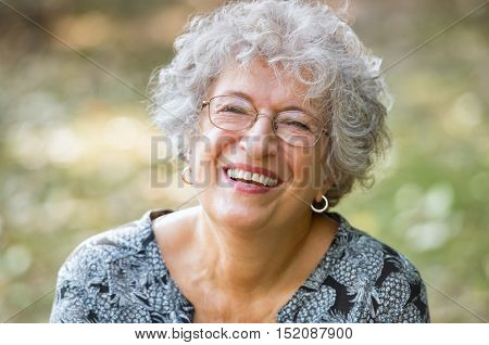 Portrait of senior woman smiling and looking at camera. Cheerful mature woman wearing eyeglasses in the park. Happy old woman with grey hair smiling. Carefree and positive retired woman.