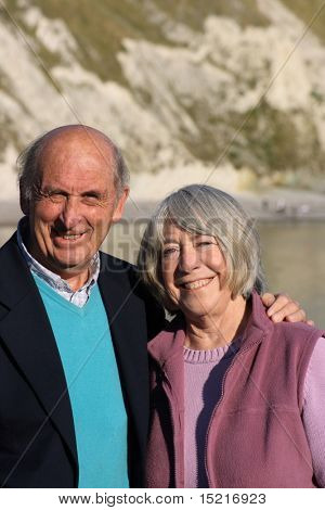 Mature smiling couple with sea and coast in the background.