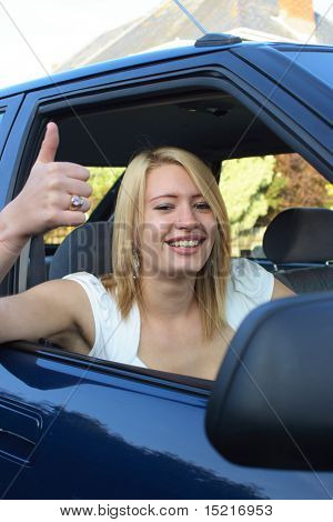 Happy teenager gives a smile and a big thumbs up seated in a car after passing her driving test.