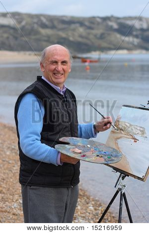 Mature artist painting a coastal landscape with paintbrush, easel and painter's palette.