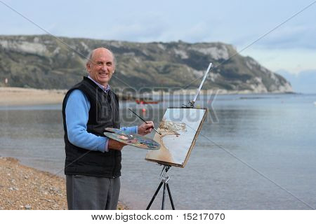 Mature artist painting a coastal landscape with paintbrush, easel and painter's palette.