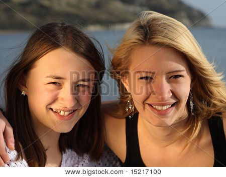 Two sisters embrace and smile on holiday by the sea.